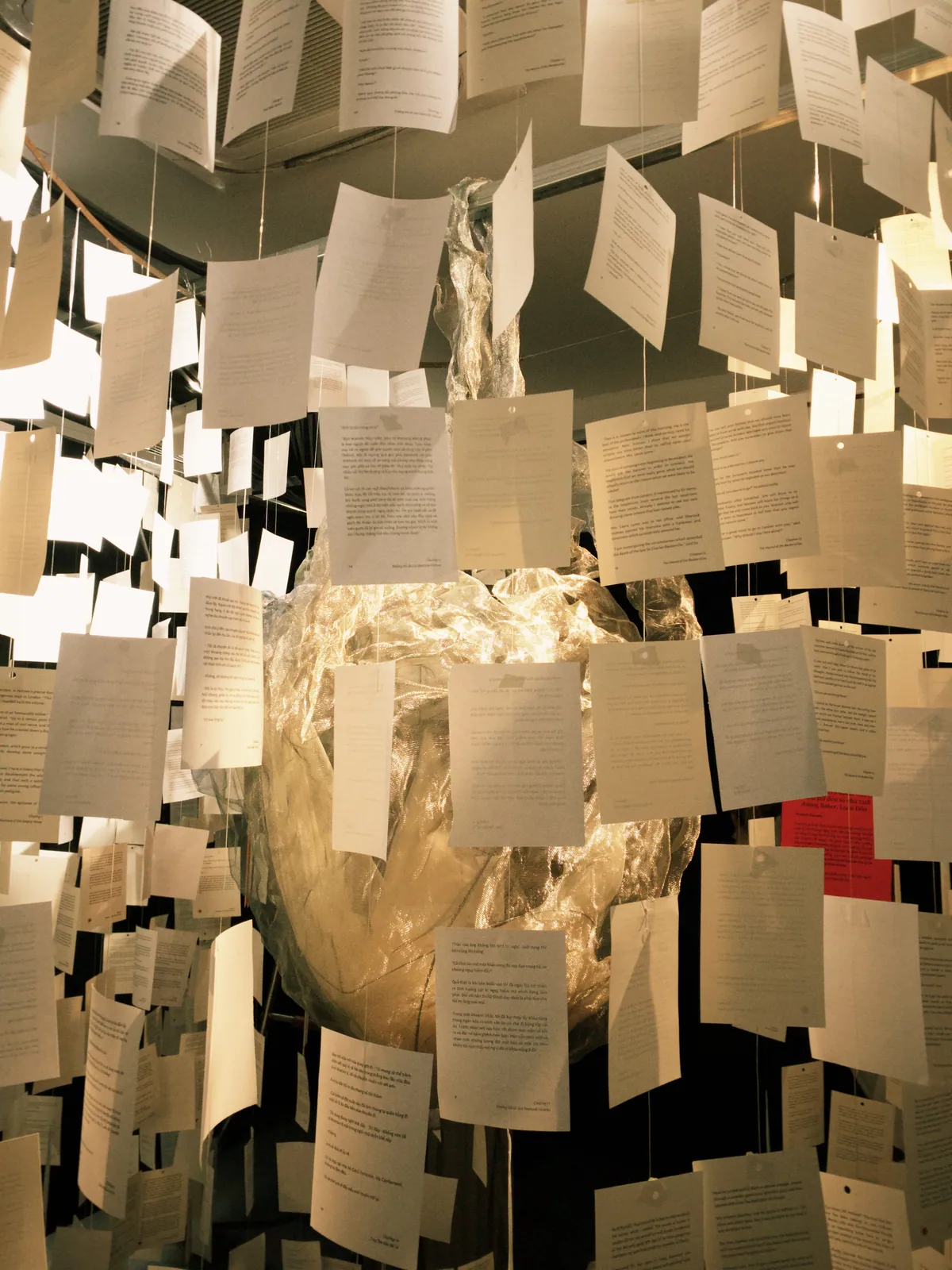 Hundreds of printed pages hung on strings around a glowing mesh-fabric form at the Light and Shadow exhibition
