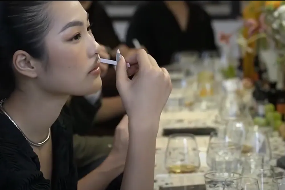 Une jeune femme sent une mouillette près d’une longue table dressée de verres et de fleurs, lors d’une dégustation de parfums