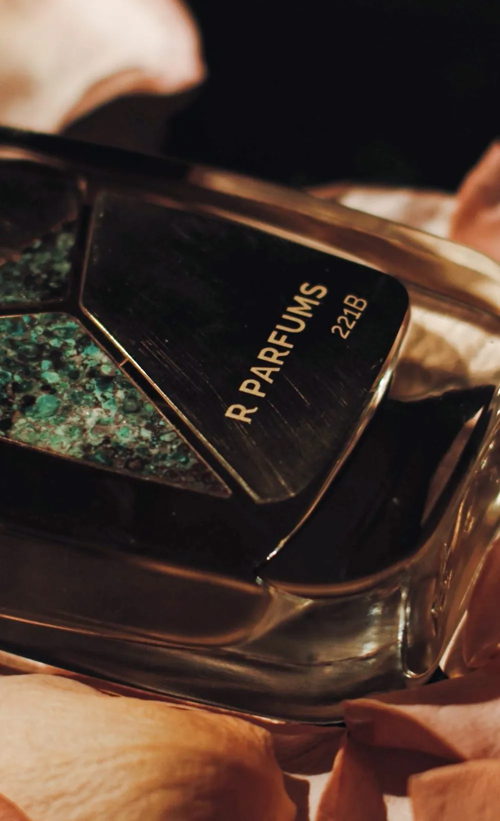 A 221B Patina bottle among pale rose petals in the dark, its name written across the frame