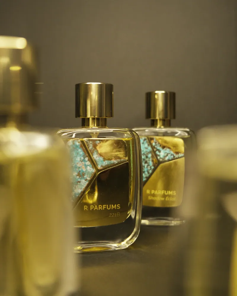 R Parfums 221B and Shadow Éclat bottles side by side, each fronted by a turquoise patina brass plate, gold caps