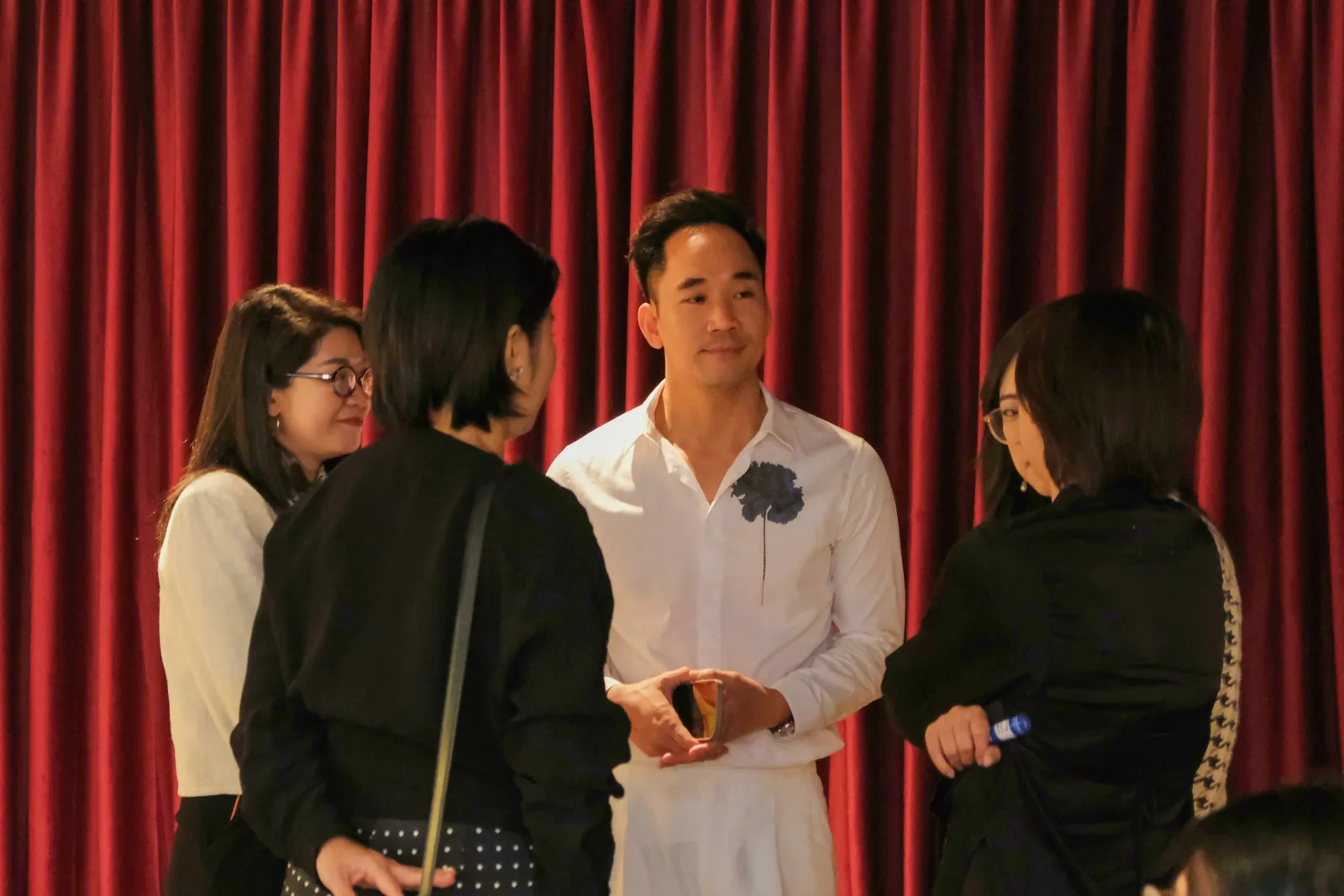 Perfume Talk のあと、赤いベルベットのカーテンの前で白い服の男性を囲んで話す来場者