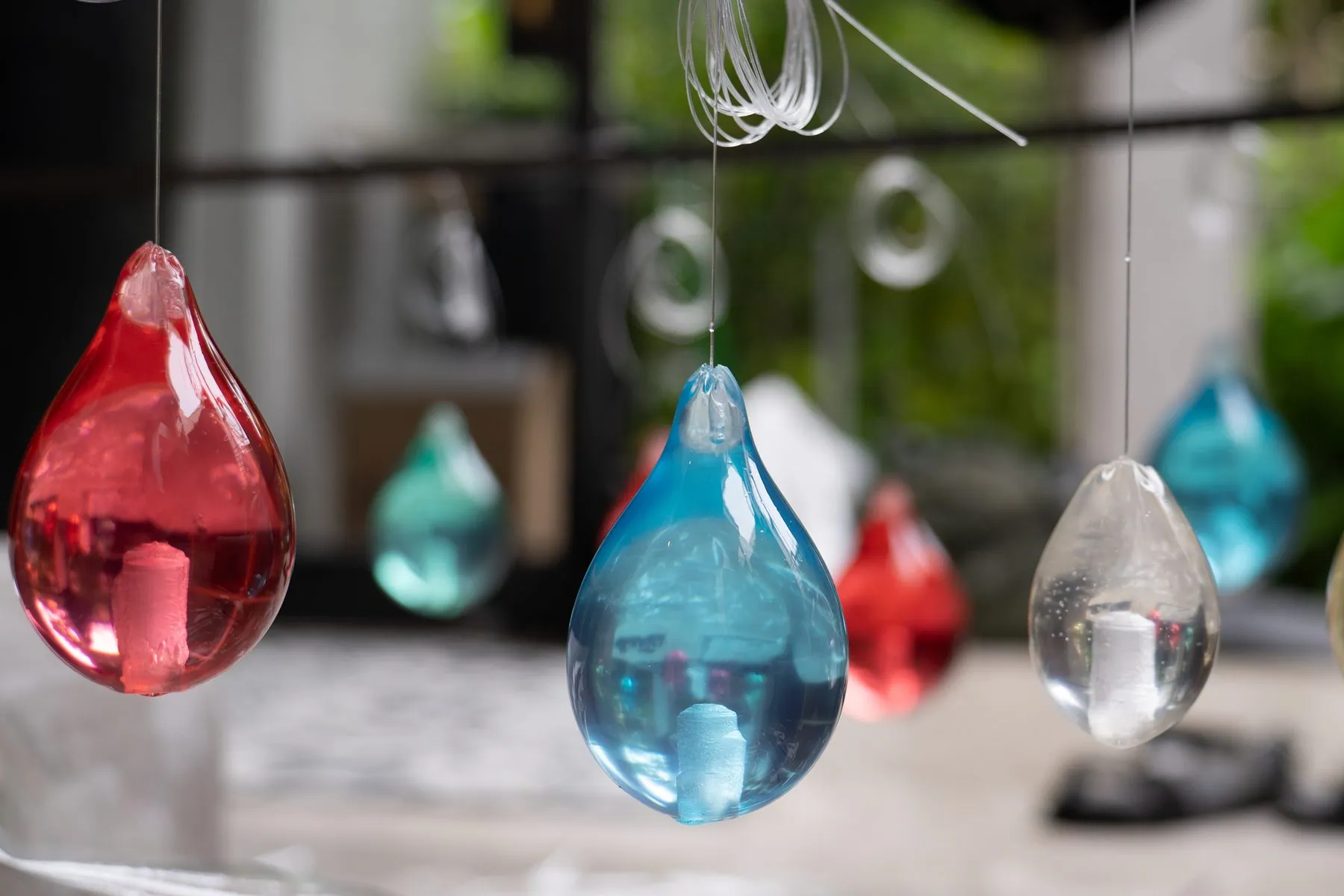 Red, blue and clear glass raindrops hanging on threads, in daylight