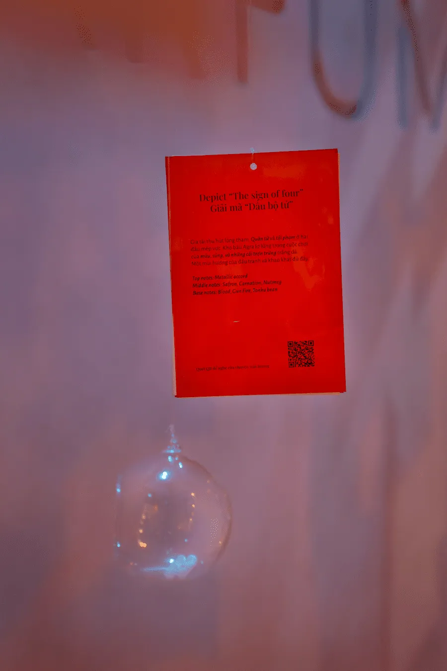 A red card titled “Decoding The Sign of Four”, listing scent notes, hung on a glass sphere at the Light and Shadow exhibition