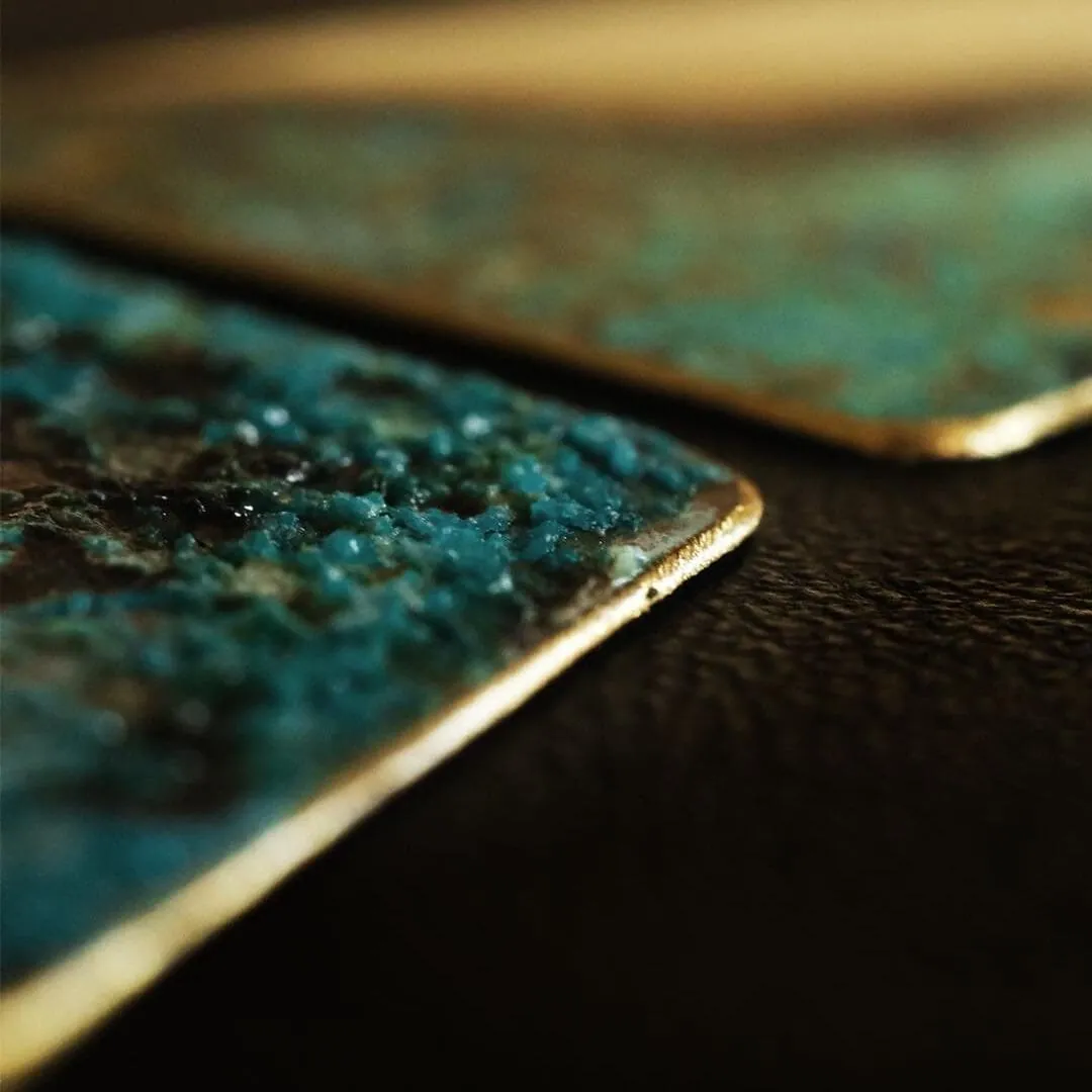 Cận cảnh hai mảnh đồng phủ Patina xanh lam kết tinh, viền kim loại vàng ánh trên nền tối