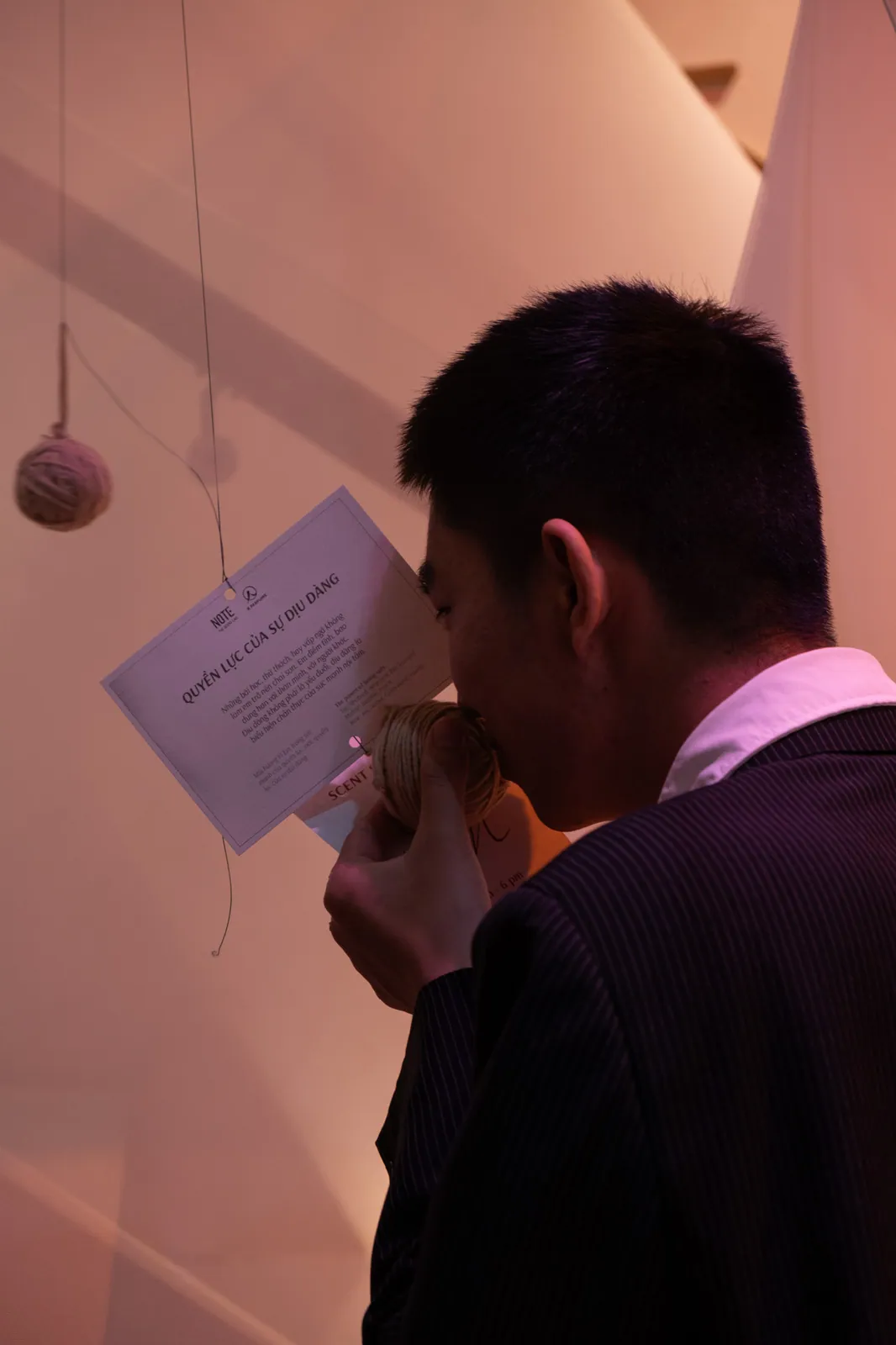 Un visiteur sent une pelote de laine près d’une carte suspendue où l’on lit, en vietnamien, « Quyền lực của sự dịu dàng » (le pouvoir de la douceur), dans une exposition olfactive
