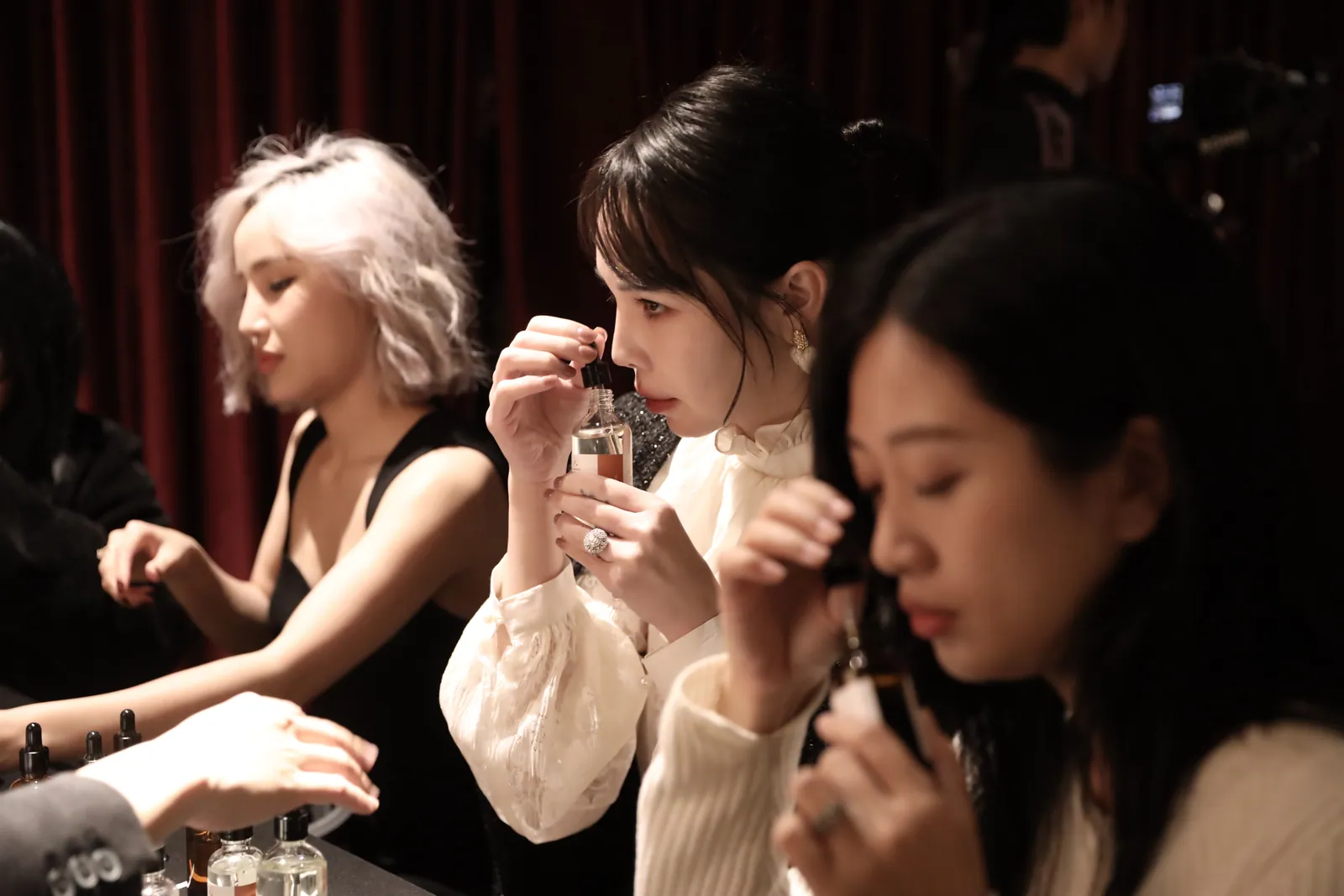 Des invités assis à une table hument de petits flacons compte-gouttes pour sentir une à une les matières premières, au vernissage de « Light and Shadow »