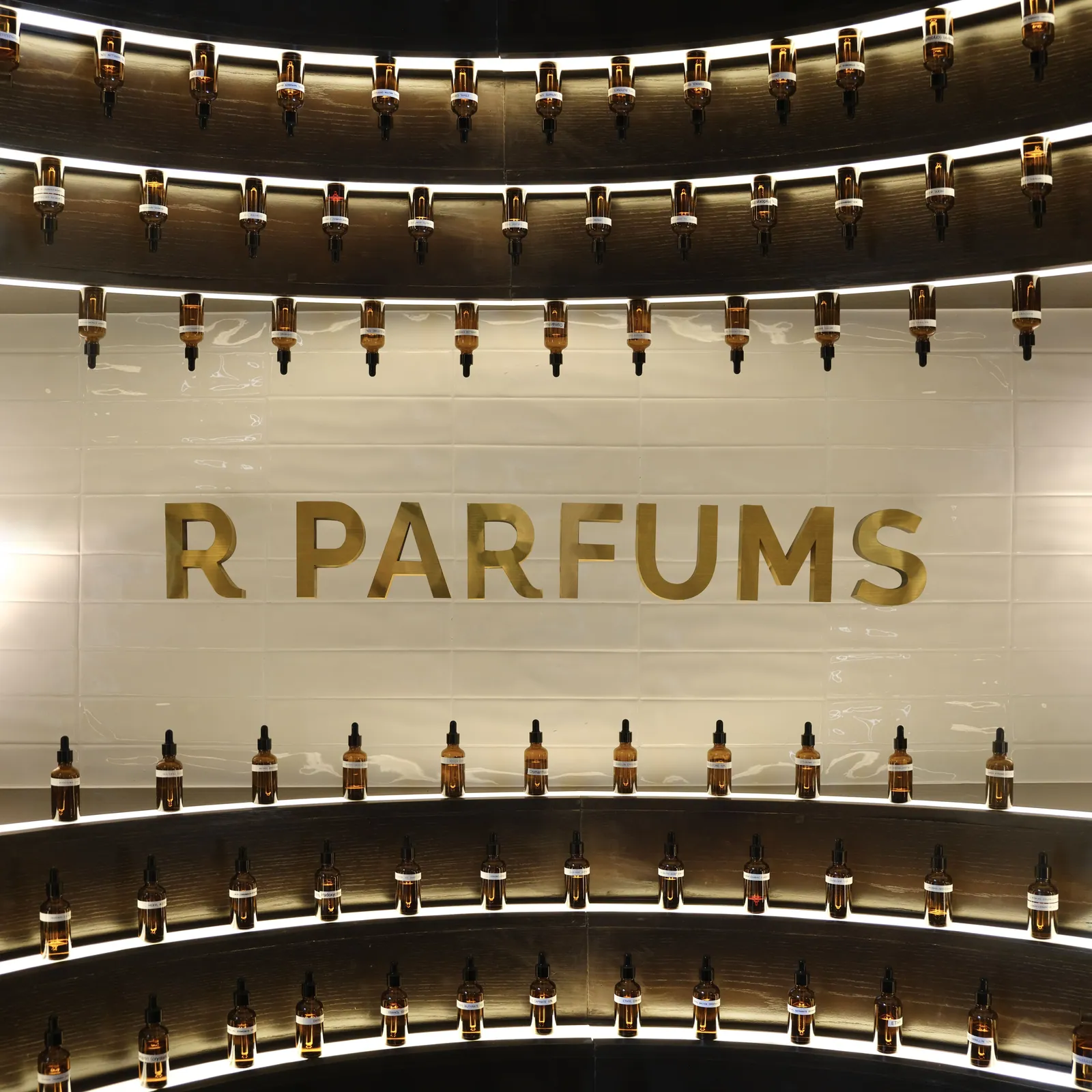 照明に浮かぶ曲線の棚。琥珀色のスポイト瓶に入った香料が、真鍮の R PARFUMS の文字を囲む