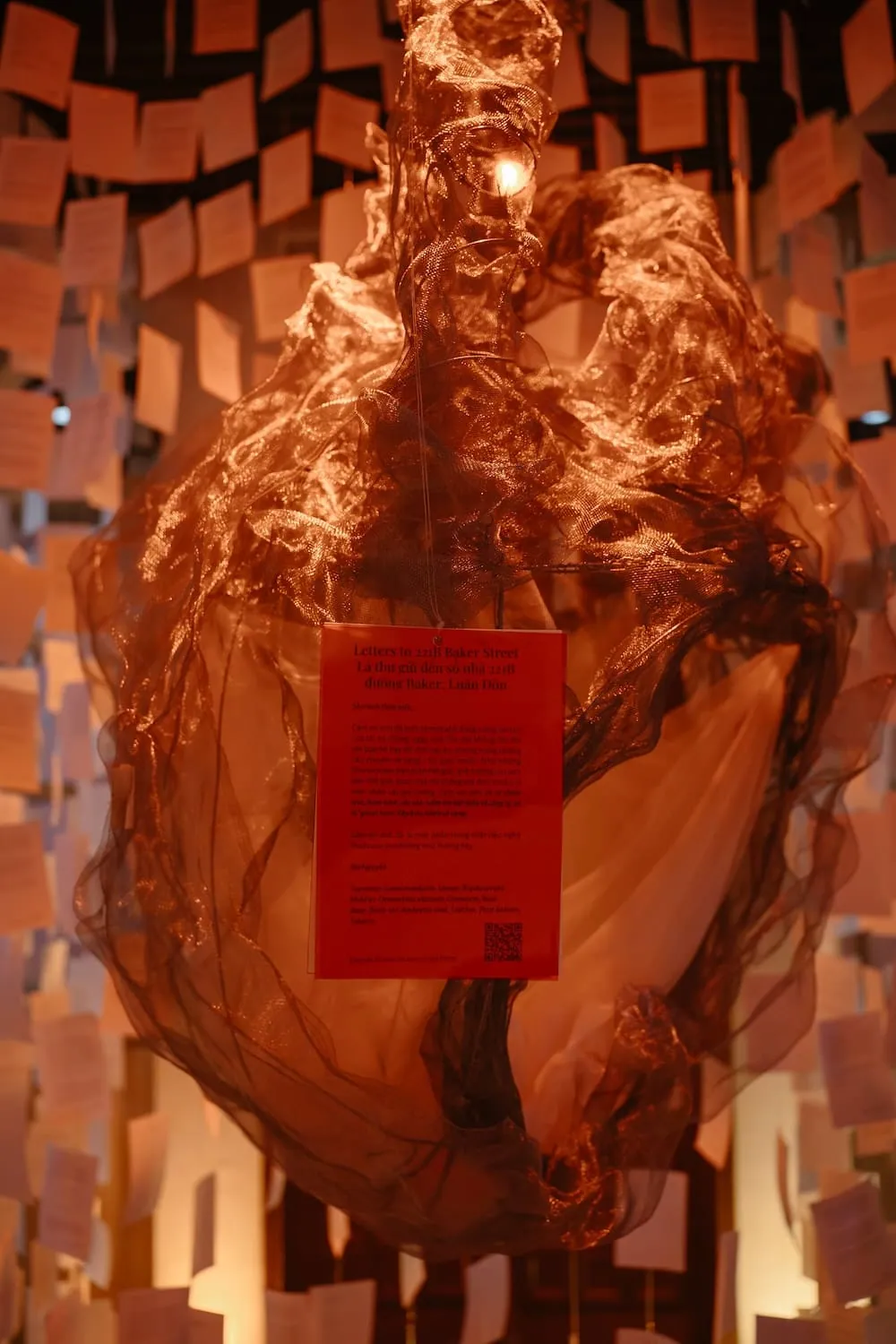 A glowing copper-red mesh form among hanging pages, with a red card reading “Letters to 221B Baker Street”