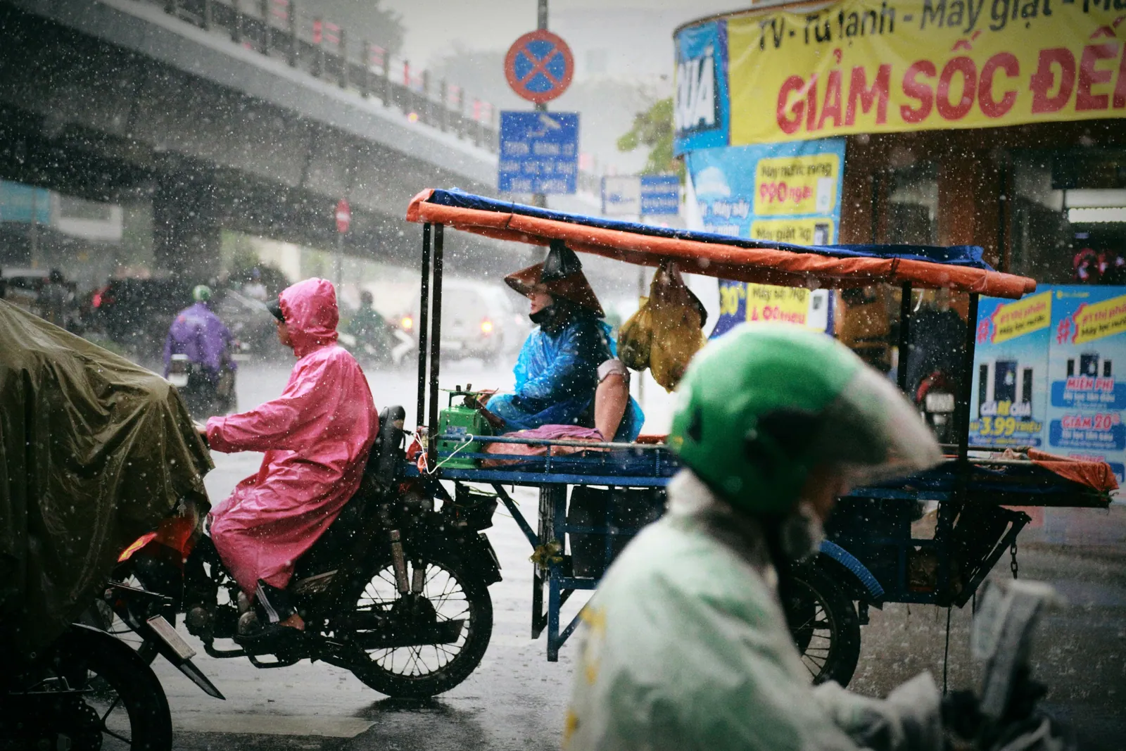 Phố Sài Gòn trong mưa: người mặc áo mưa hồng chạy xe máy, xe đẩy hàng rong che bạt dưới cầu vượt