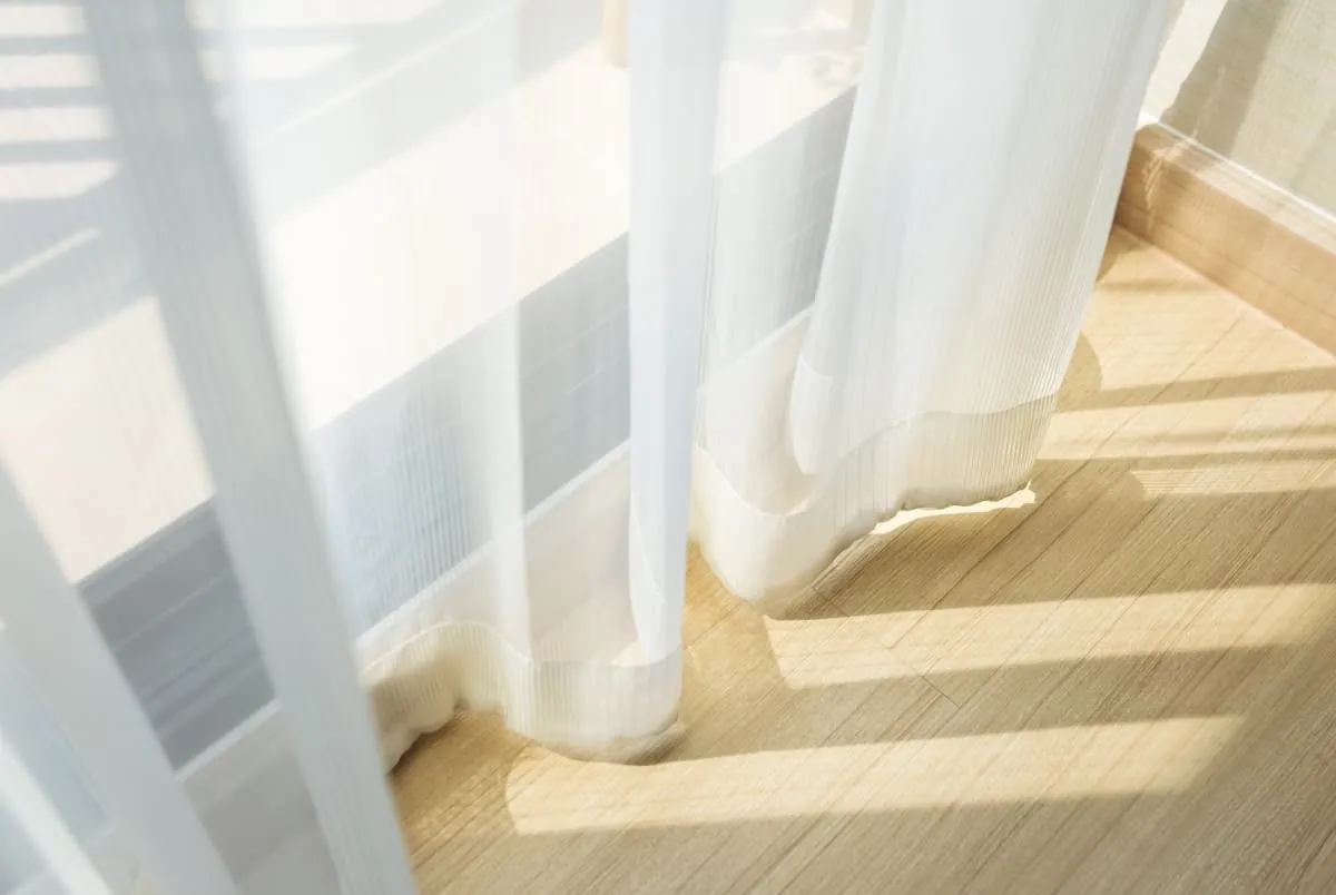 Voilage blanc qui bouge à peine près d’une fenêtre, le soleil traçant des bandes sur un parquet – un moment de calme