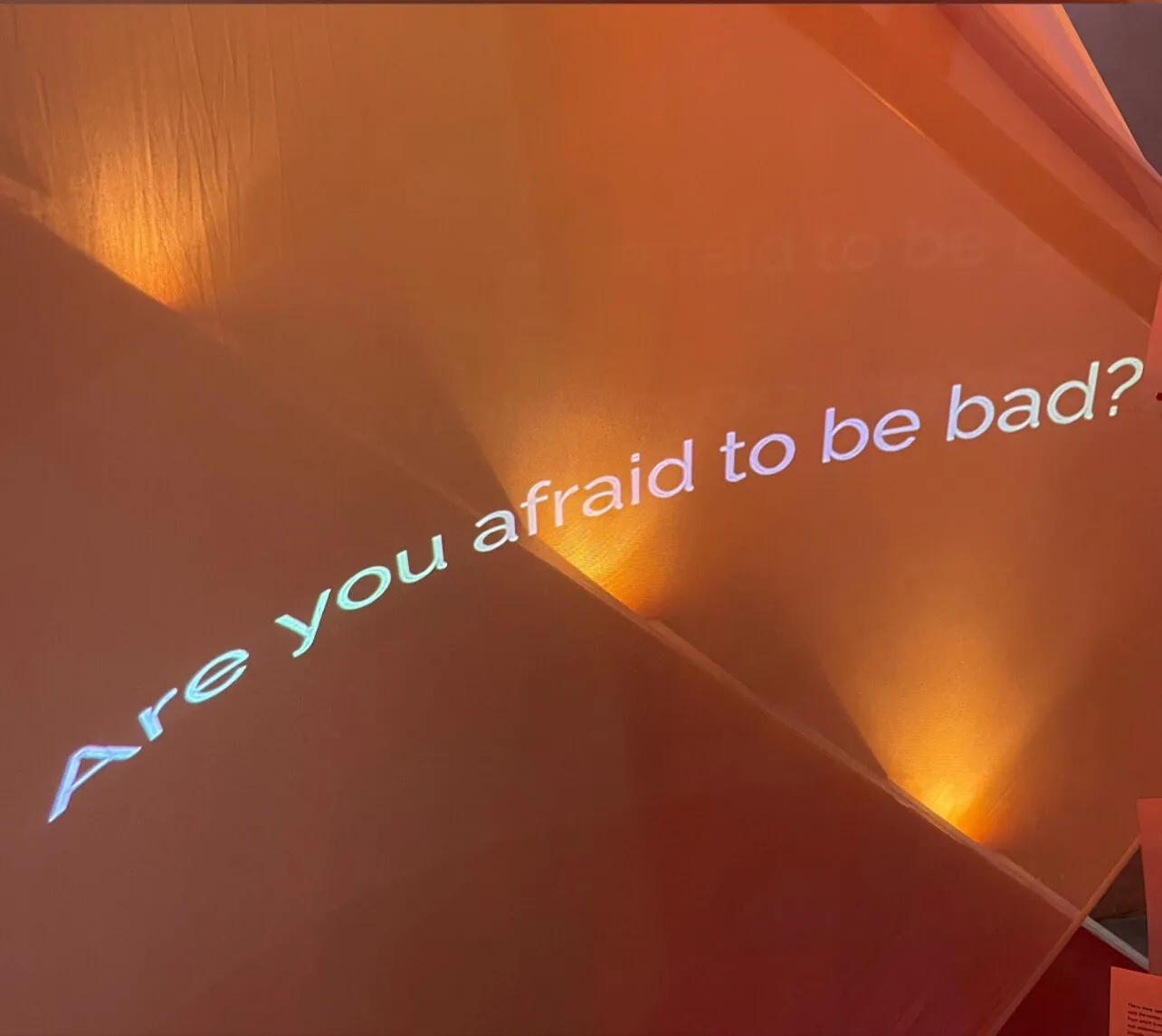 La phrase « Are you afraid to be bad? » projetée sur une toile tendue, dans une lumière orange, à « Light and Shadow ».