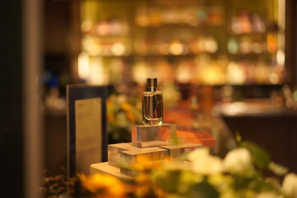 R Parfums bottle on clear acrylic blocks among soft flowers, bar lights glowing behind, at Oku restaurant