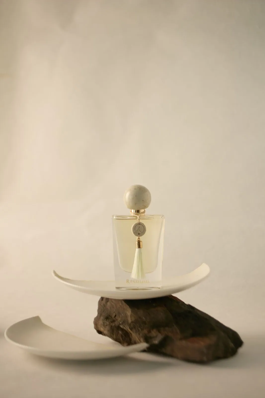 A Ceramic bottle with a speckled cap, white tassel and R charm, on a broken ceramic plate and a stone