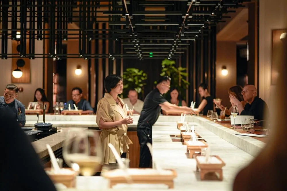Rei Nguyen, une mouillette à la main, près du long comptoir en pierre d’un restaurant, lors d’un événement associant parfum et gastronomie