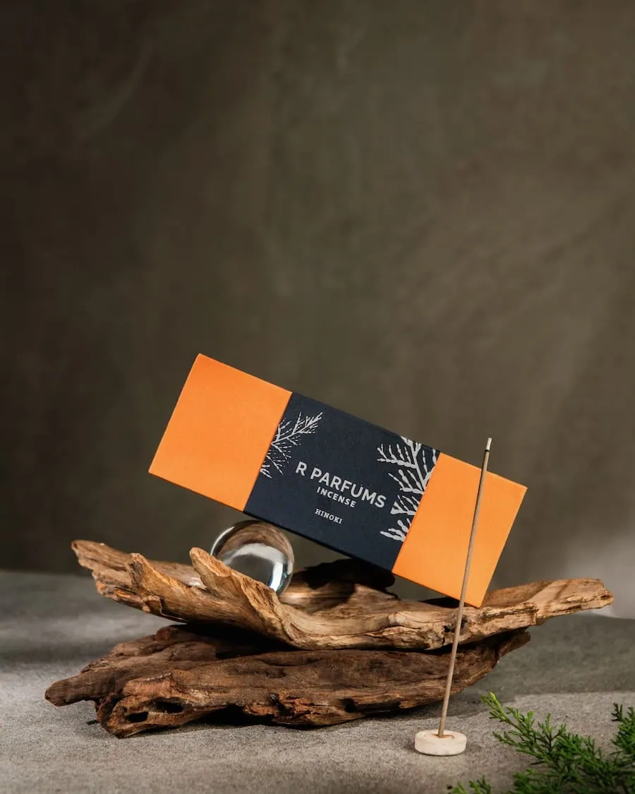 R Parfums Incense Hinoki 香盒置於漂流木上，旁有一顆玻璃球與一支線香。
