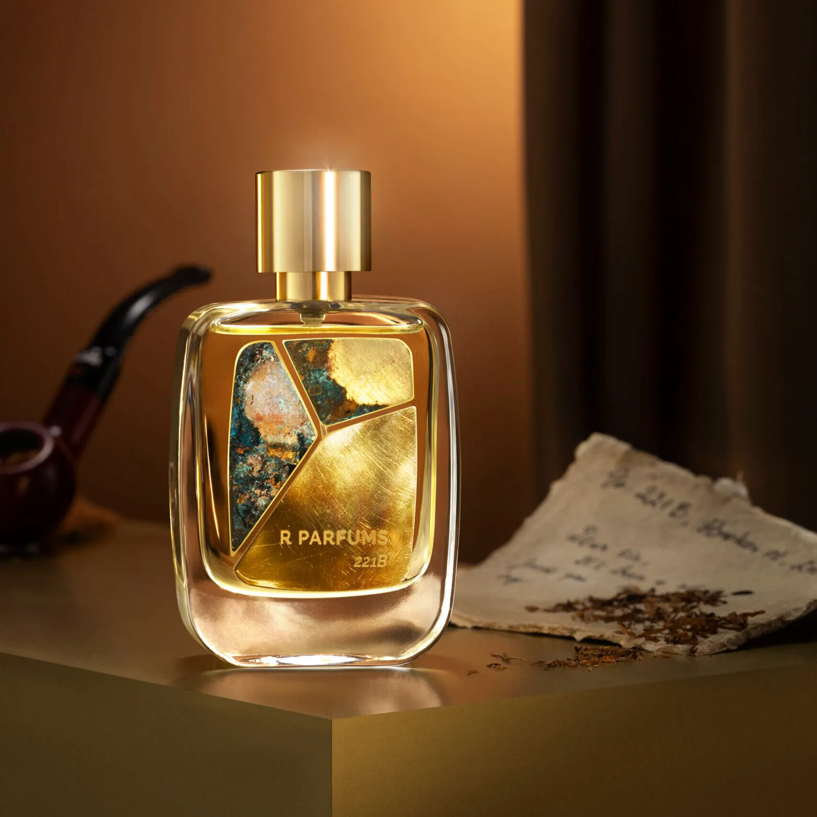 真鍮のパティナをあしらった R Parfums の 221B のボトル。パイプ、刻みたばこの葉、古い手紙とともに、温かな黄色い光のなかに置かれている