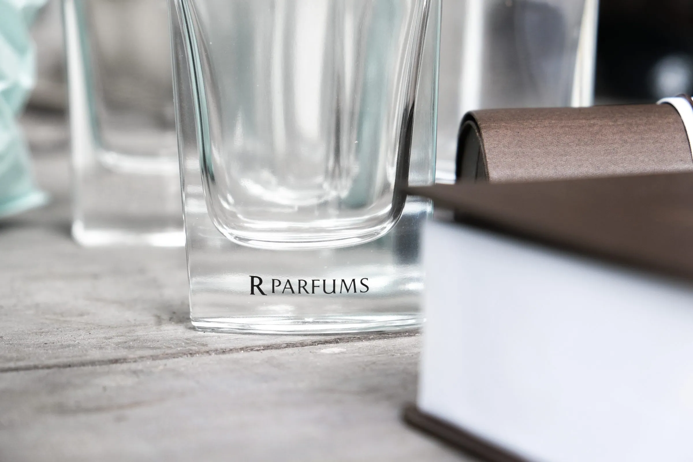 A square glass bottle engraved with R PARFUMS beside a brown box