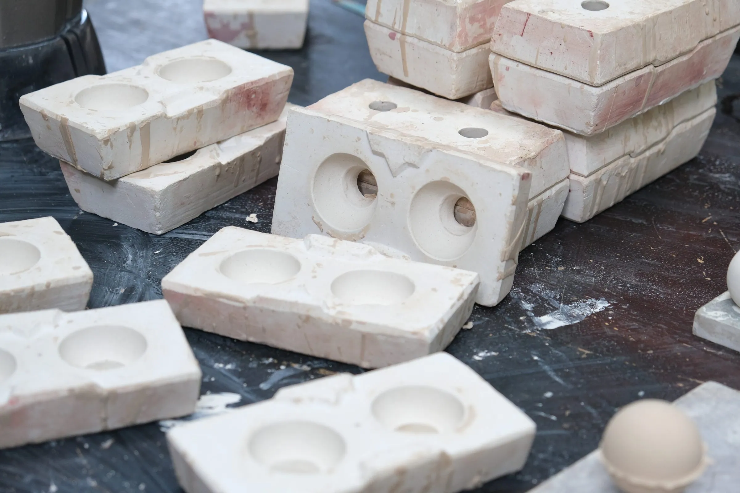 Opened white moulds stacked together, their round hollows showing, a cream sphere resting in one corner