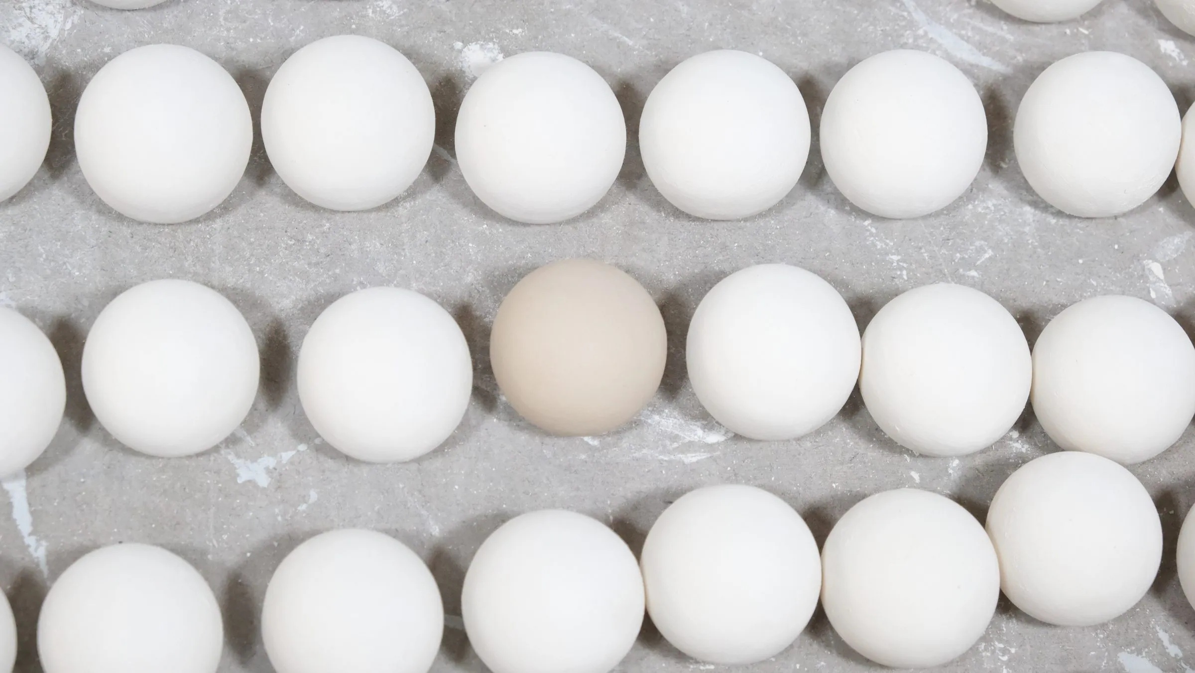 Three straight rows of white spheres drying on a board, one cream sphere in the middle row