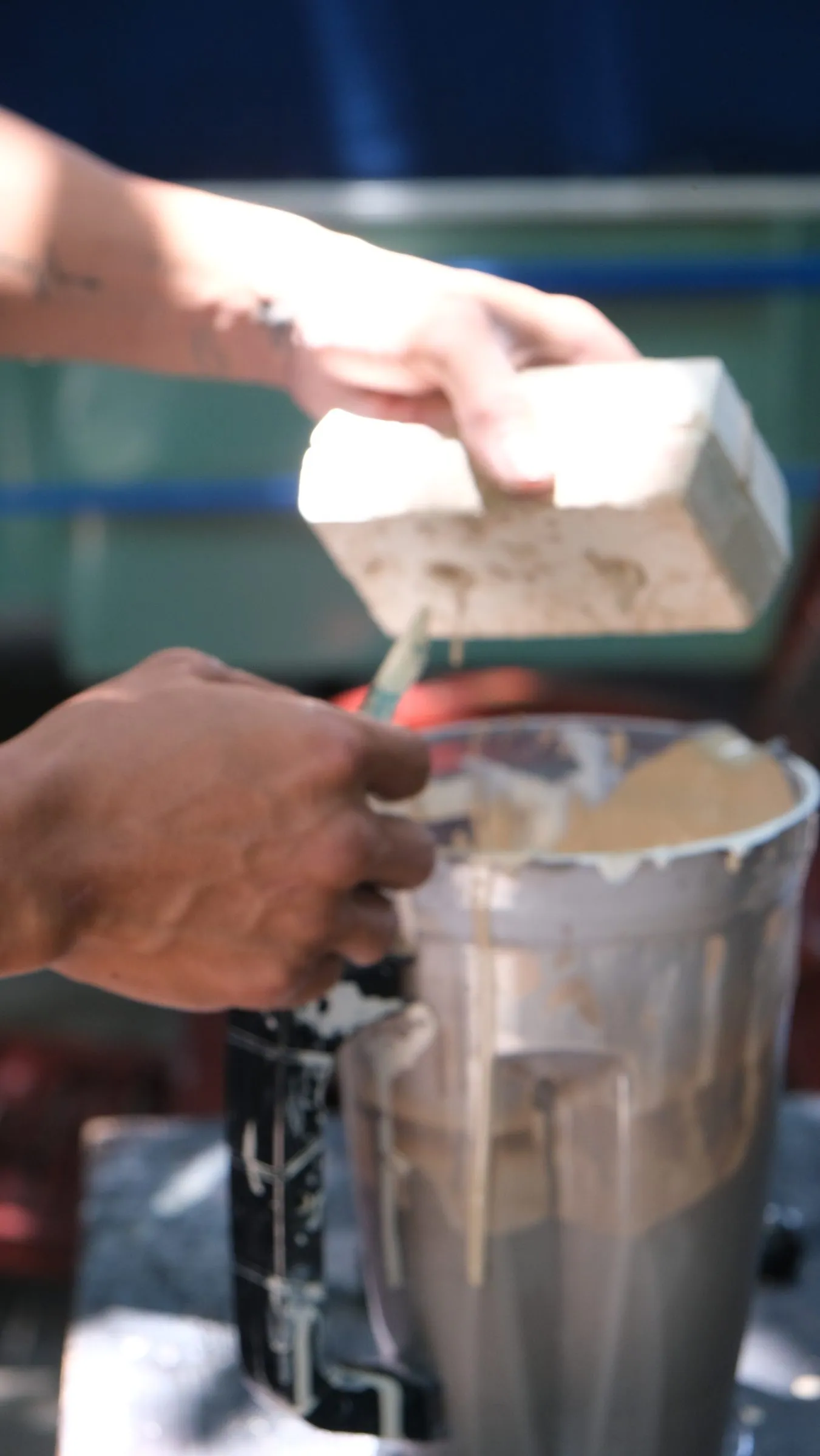 Hands tipping a white mould over a jug, the excess liquid clay running out, against a blue background