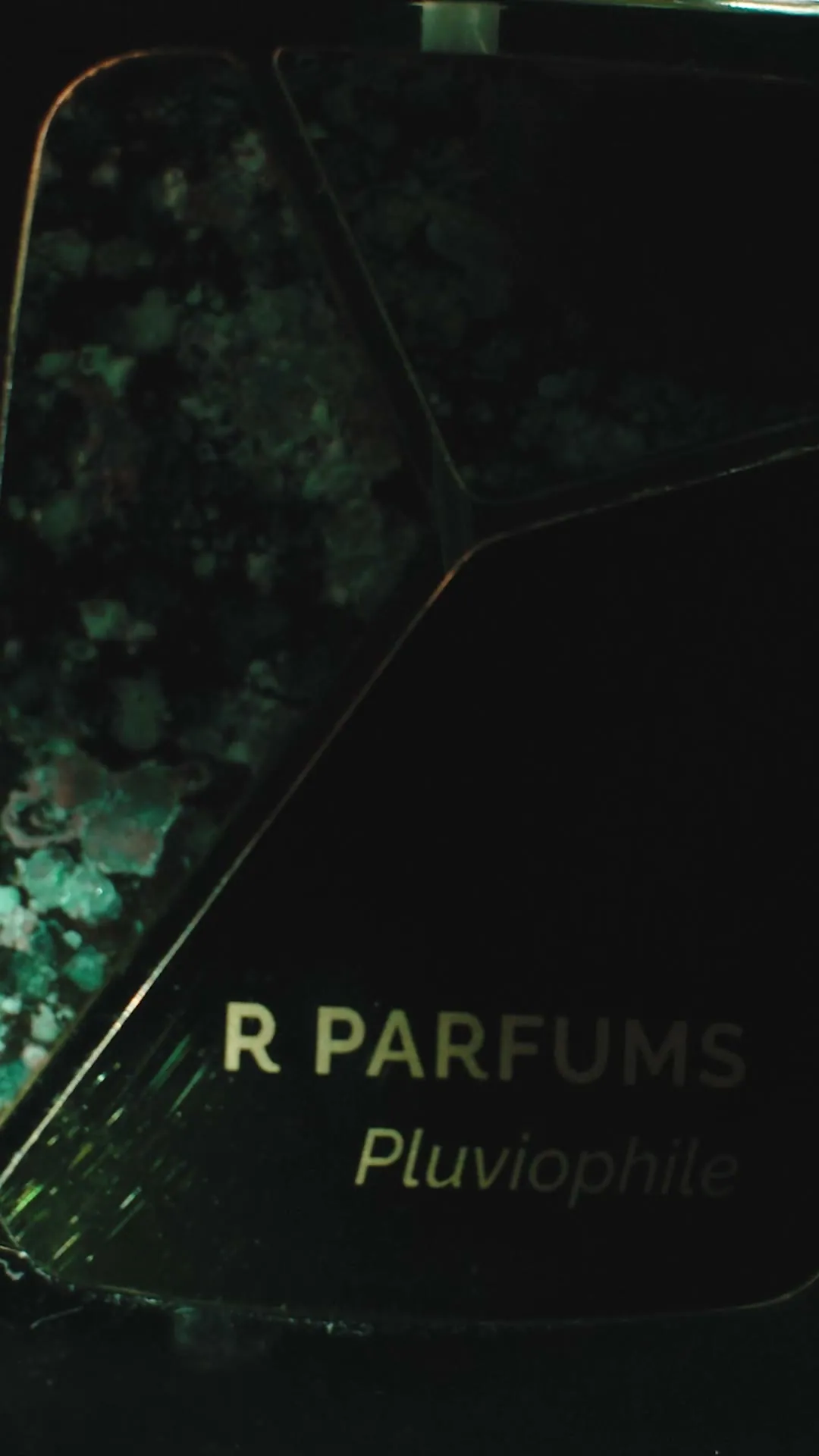 Still from the 2022 film: the brass pieces of a Pluviophile Patina bottle in close-up, green patina flecked across one and ‘R PARFUMS Pluviophile’ on another