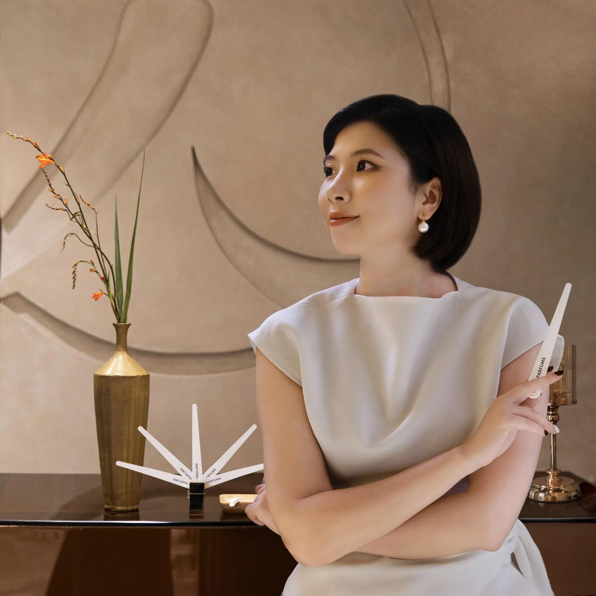 Rei Nguyen in a white top, holding a scent strip; in front of her, a fan of strips on a stand and a brass vase of orange flowers