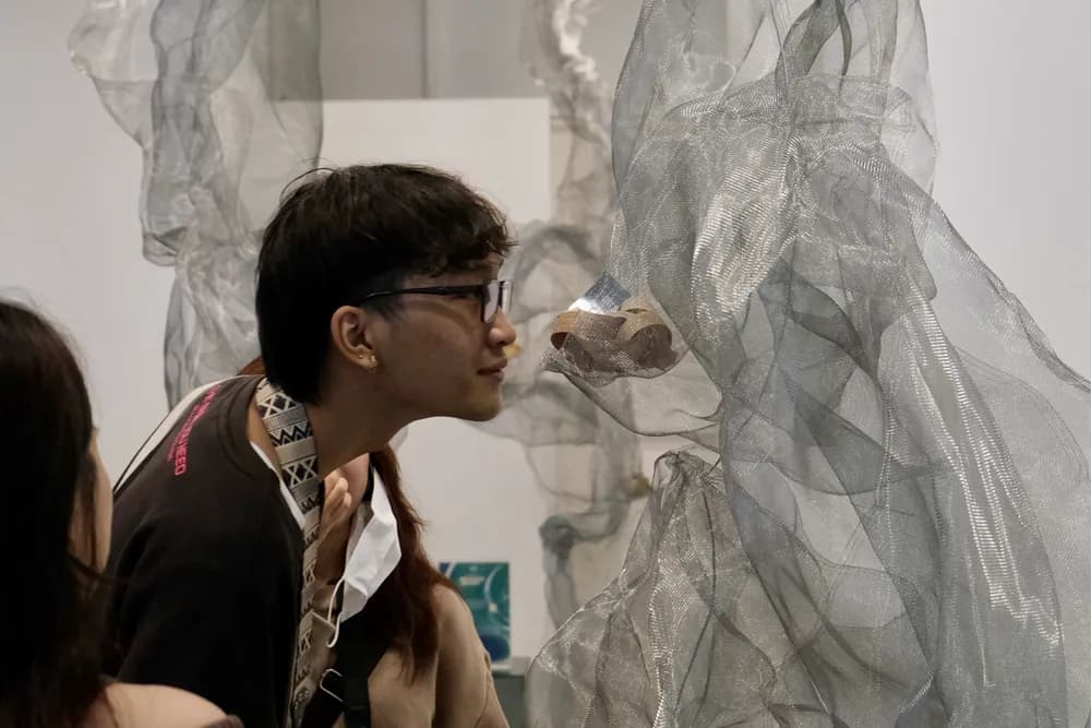 观展者凑近嗅闻一件小物，它摆在灰色金属网构成的装置之间，摄于嗅觉艺术展。