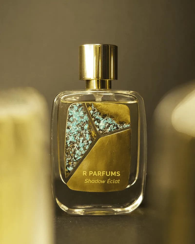 Chai Shadow Éclat của R Parfums, tấm đồng thau patina xanh ngọc lốm đốm sẫm màu trên mặt chai, nền tối