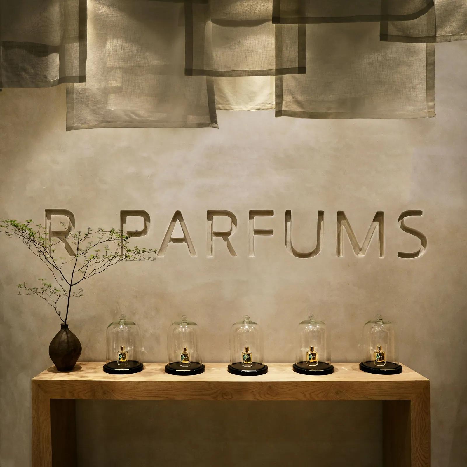 R PARFUMS carved into a plaster wall above five bottles under glass cloches on a wooden console