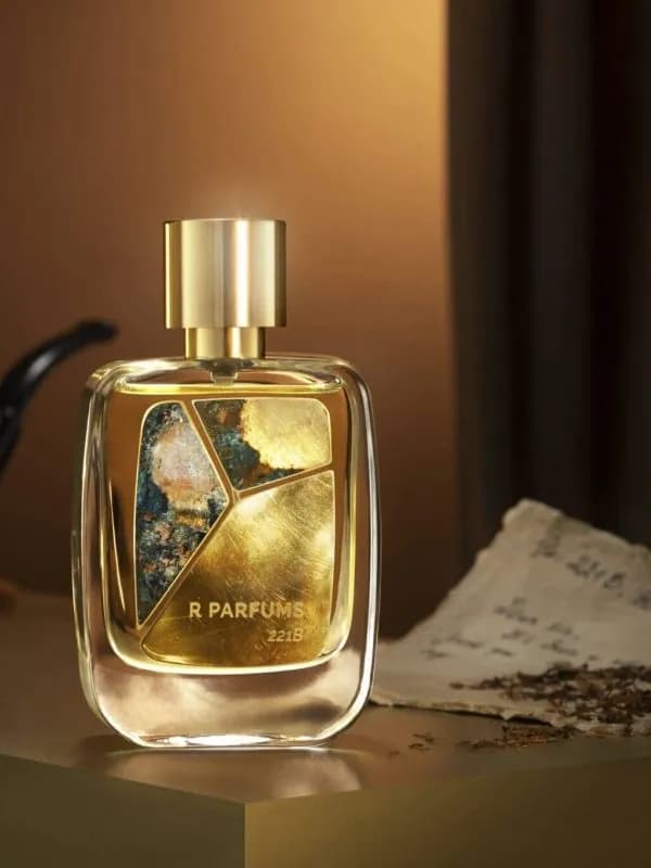 Chai 221B của R Parfums trong căn phòng ánh đèn ấm, cạnh tẩu thuốc và lá thư tay rắc vụn thuốc lá