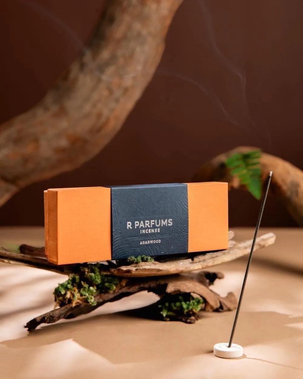 R Parfums Incense Agarwood box on mossy driftwood, a thin thread of smoke rising from the stick