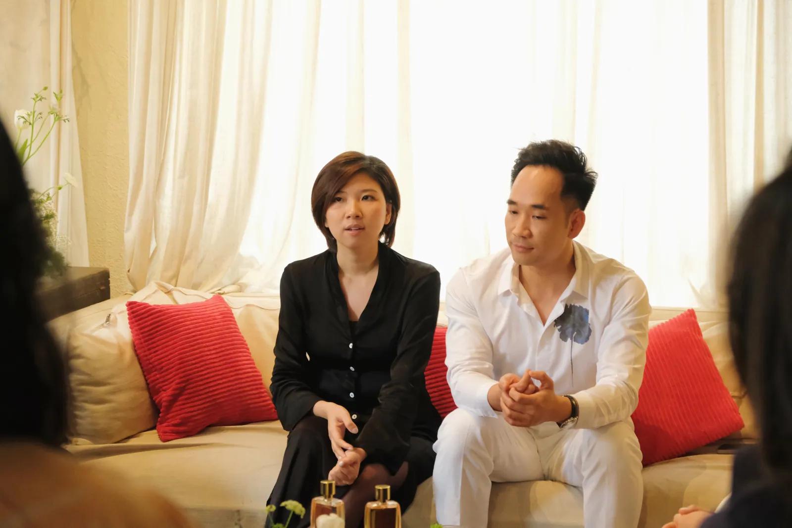 Rei Nguyễn (trái) và Nguyễn Quốc Huy (phải) ngồi sofa nệm đỏ trò chuyện tại Perfume Talk, trước mặt là chai nước hoa