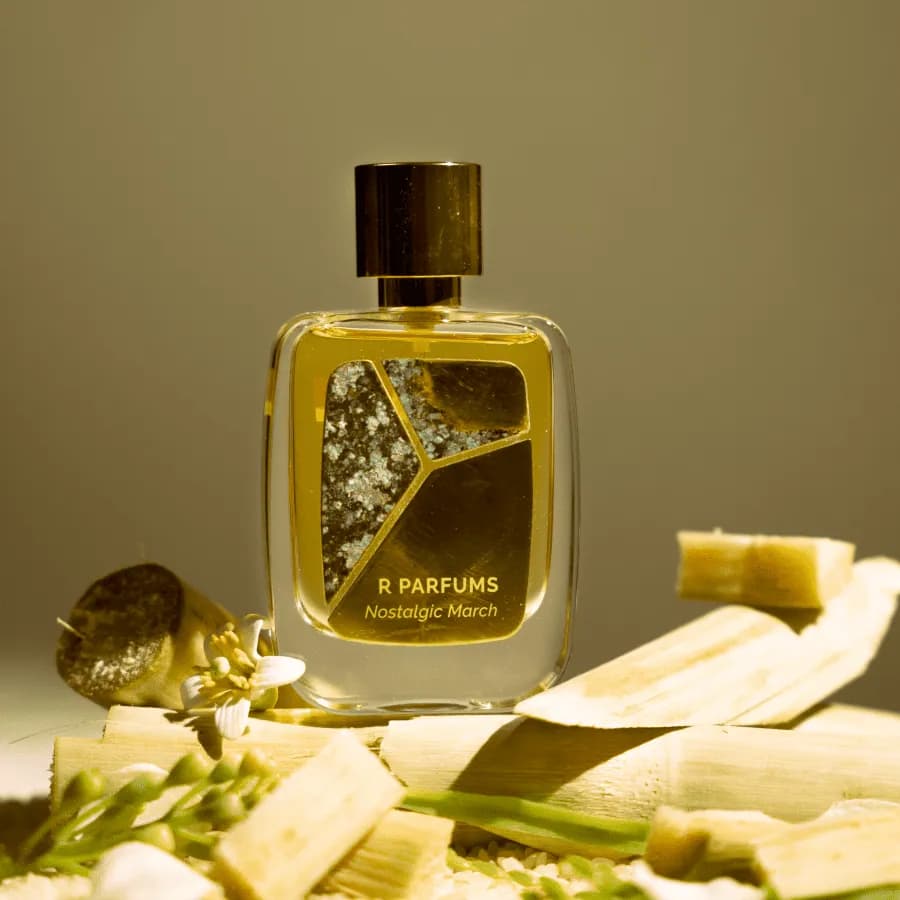 R Parfums Nostalgic March 香水瓶立在几段甘蔗上，旁有一朵白色柚子花，沐浴在温暖的阳光里。