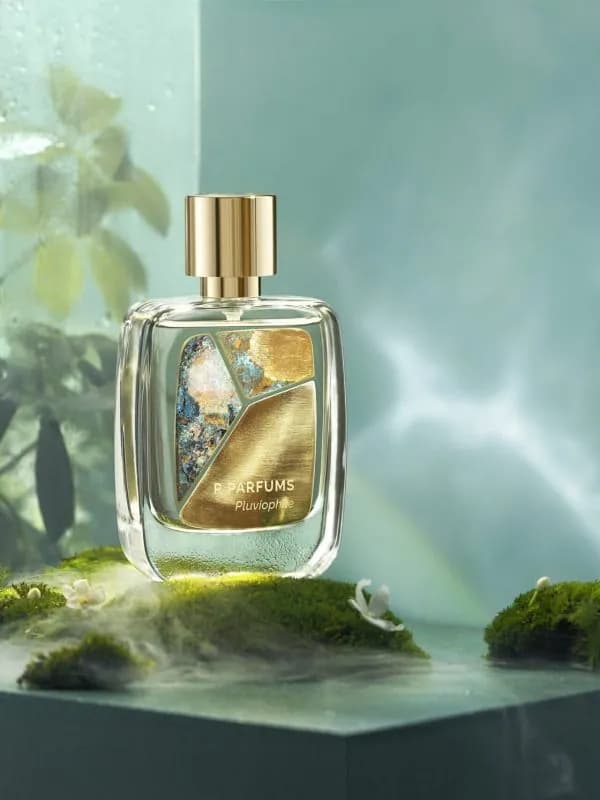 Chai Pluviophile của R Parfums trên nền rêu ẩm, sương mờ và lá xanh sau ô kính đọng nước mưa