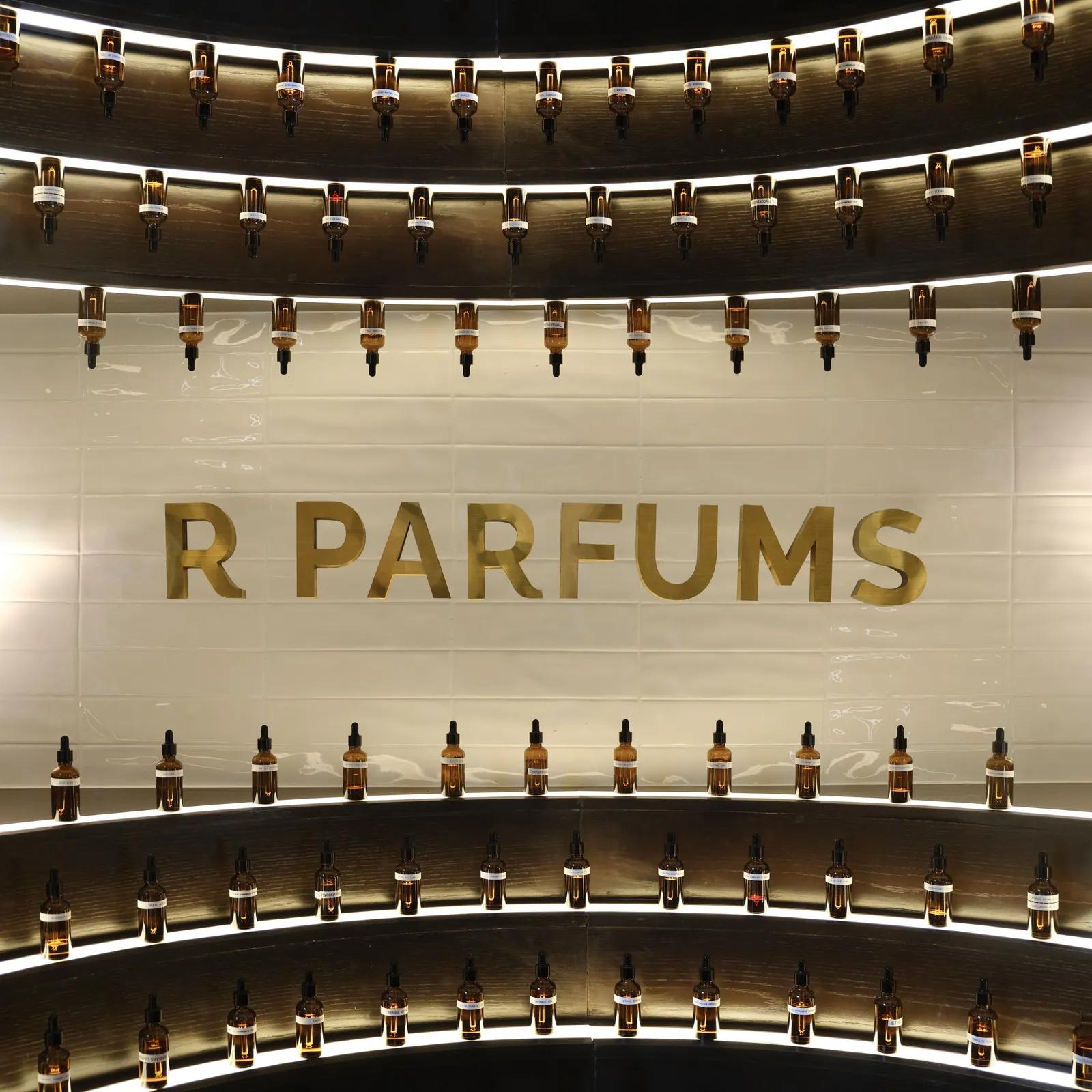 Lit curved shelves of amber dropper vials of raw materials around brass R PARFUMS lettering