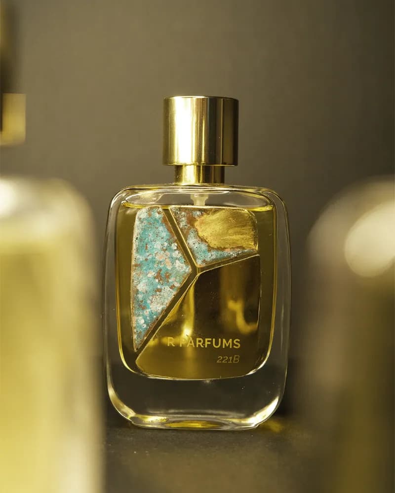 Chai 221B của R Parfums, tấm đồng thau patina xanh nhạt pha vệt vàng trên mặt chai, nắp vàng bóng