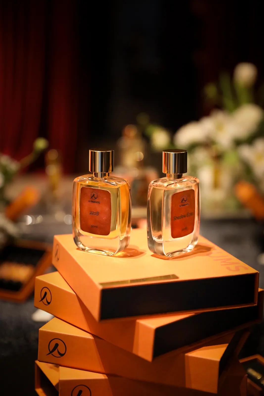 两瓶 50 ml 的 221B 与 Shadow Éclat，棕色皮革标签，立于 R Parfums 橘色纸盒堆上，摄于《Light and Shadow》嗅觉展。