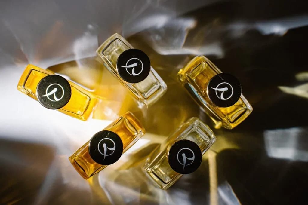 五瓶黑色瓶盖印有 R 字的 R Parfums 香水,自上方俯拍,阳光穿透瓶身,香水泛着金黄光泽。