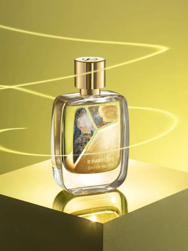 Chai Eau de Hajime của R Parfums, tấm đồng thau patina thủ công, đặt trên khối vàng giữa vệt sáng uốn lượn