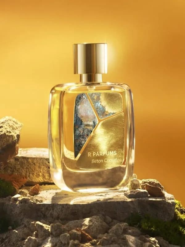 Chai Béton Chaud của R Parfums đặt trên phiến đá thô, rêu xanh, dưới ánh nắng vàng ấm