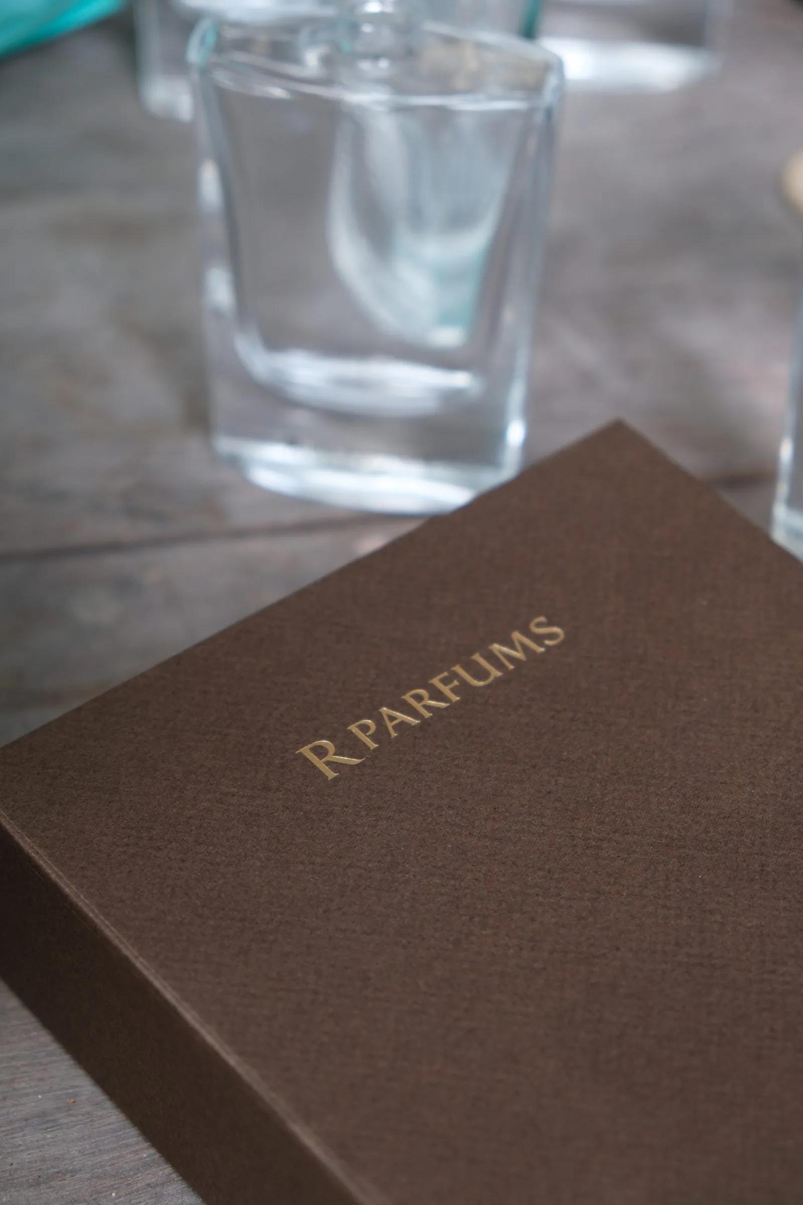 印着金色 R PARFUMS 字样的棕色盒子，后方一只透明玻璃瓶，略微失焦。
