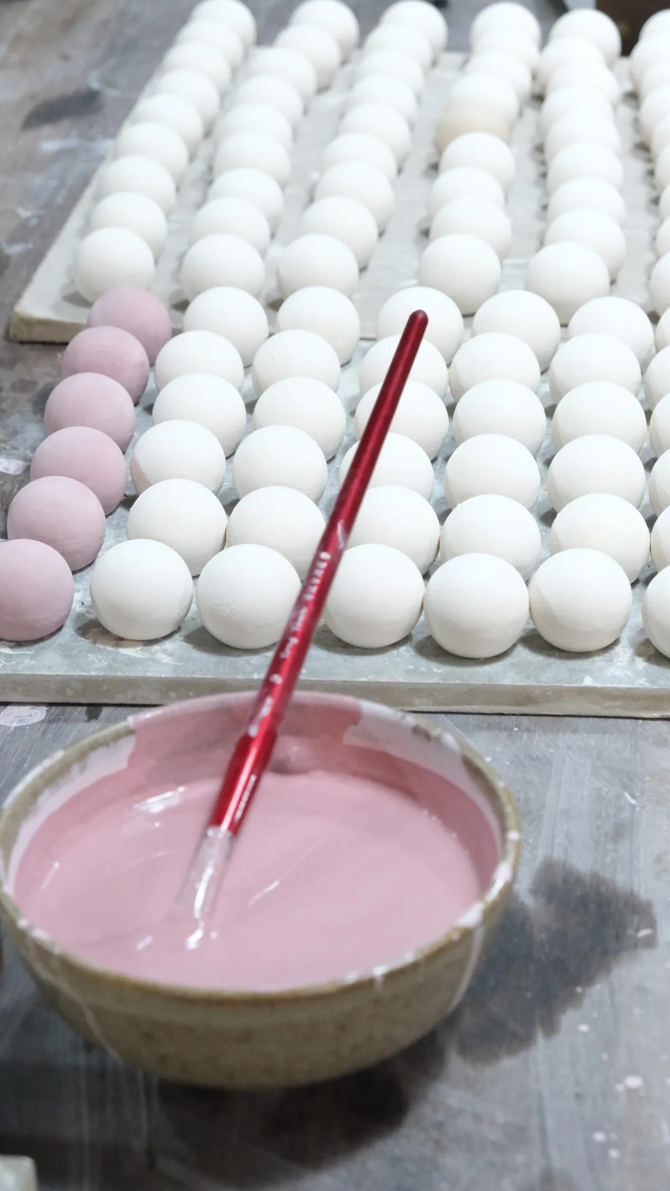 Bát men hồng có cọ cán đỏ, cạnh khay cầu trắng, hàng bên trái đã phủ hồng