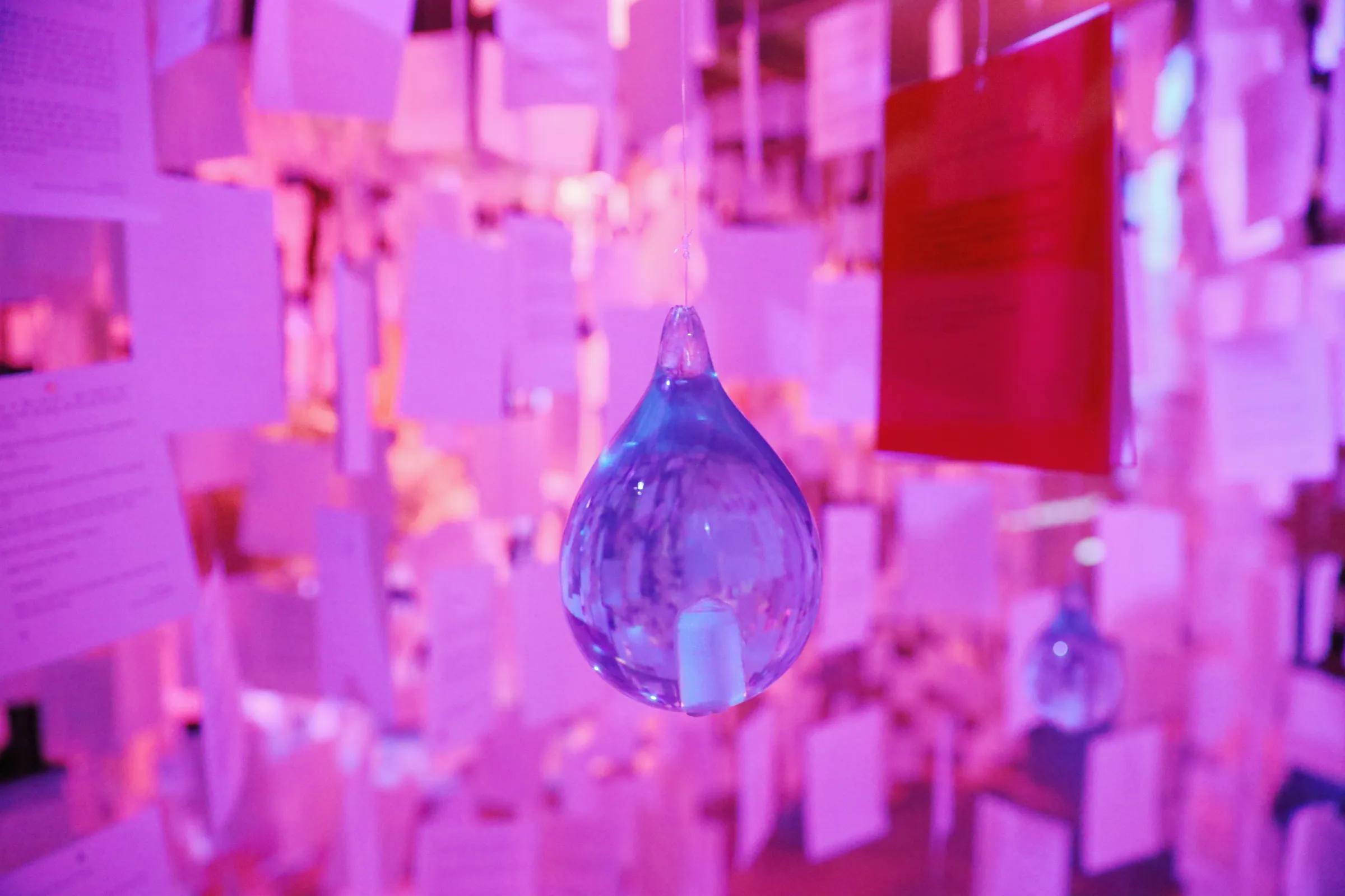 A blue glass droplet hanging among pink-violet letters, with a red card to the right