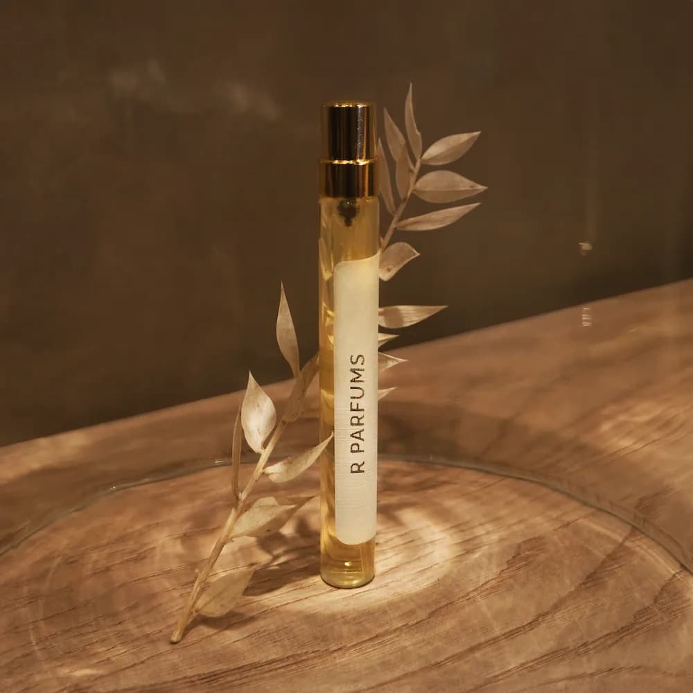 暖光中,12 ml 瓶身立在木制圆盘上,旁有一小枝干叶
