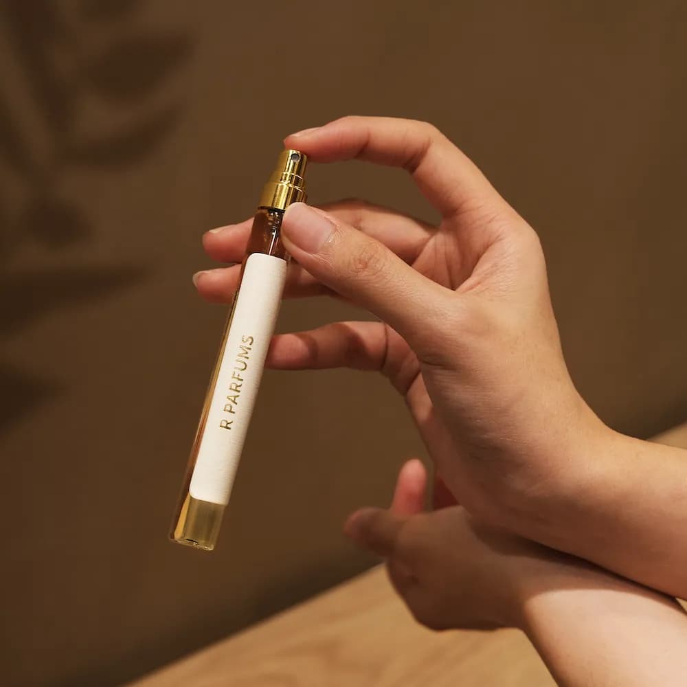 手握细长的 12 ml 小瓶，瓶身直向印着 R PARFUMS