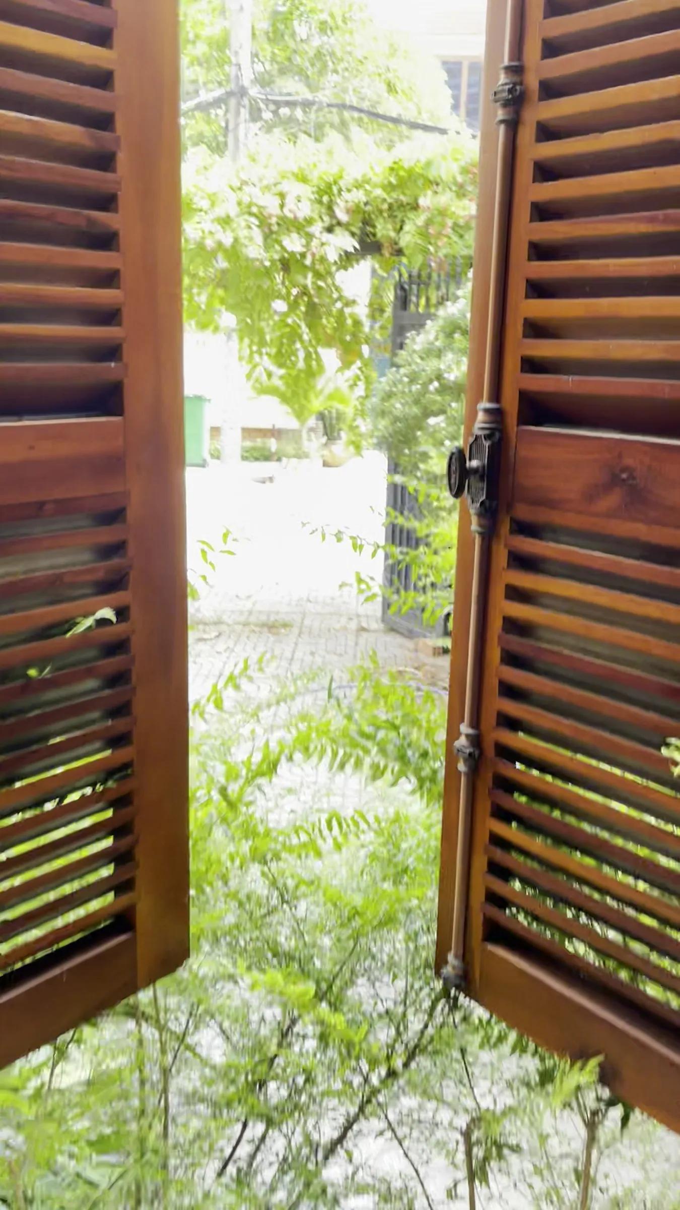 Two brown wooden shutters opening onto a green courtyard and an iron gate, in the old house before renovation