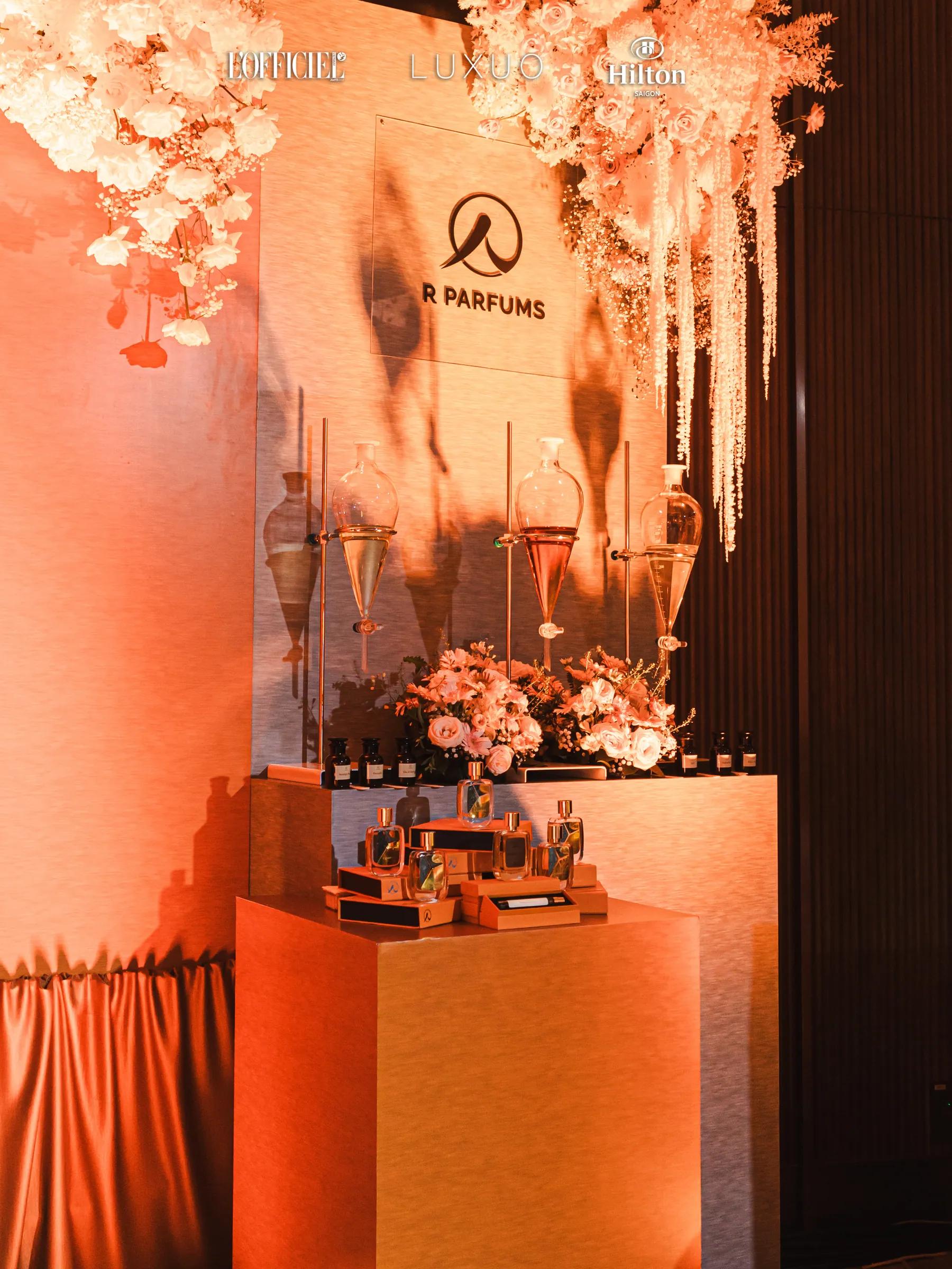 Gian R Parfums ở Wedding Symphony 2025, Hilton Saigon: ba bình phễu thuỷ tinh trên giá thí nghiệm, hoa màu hồng và trắng, chai Patina đặt trên hộp