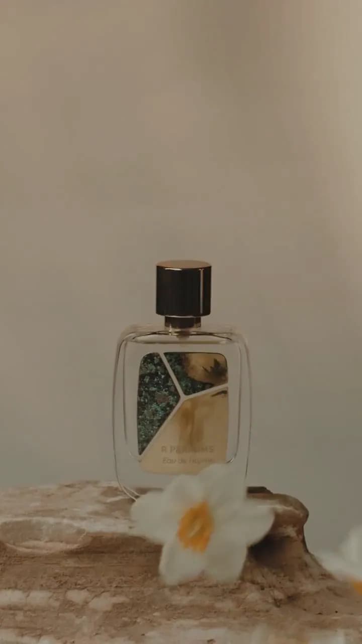 影片,2022:Patina 瓶装的 Eau de Hajime 立在石上,旁有西洋梨、白花与一只手。原配音乐,此处静音循环播放。