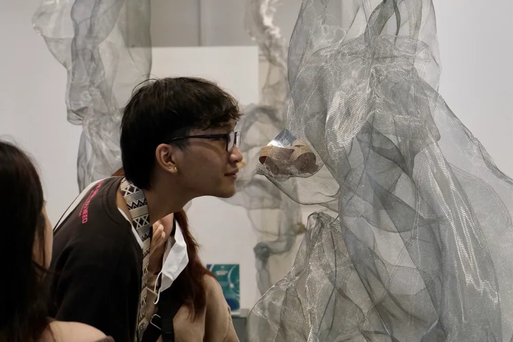 Seorang pengunjung mendekatkan diri untuk menghidu sebuah objek kecil di dalam instalasi jaring logam kelabu di sebuah pameran seni olfaktori
