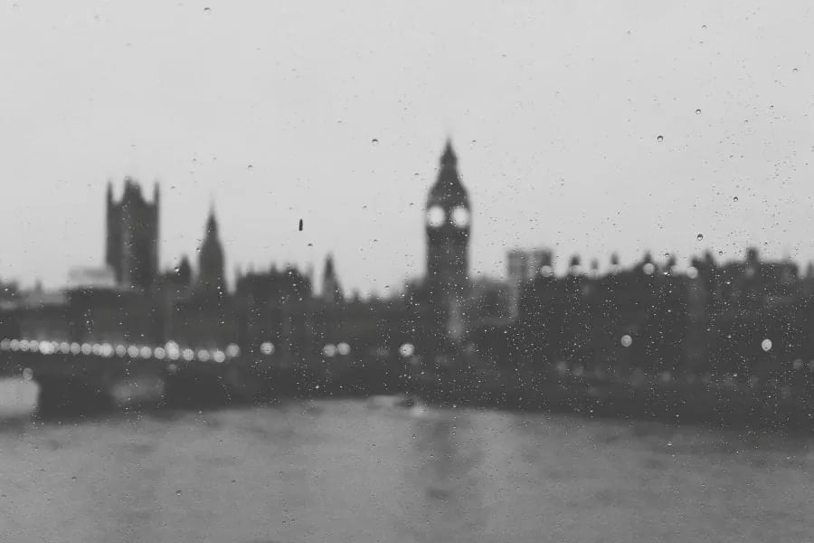 Foto hitam putih menerusi jendela yang dicoreti titisan hujan: menara jam Big Ben dan tebing sungai London yang kabur dalam kabus